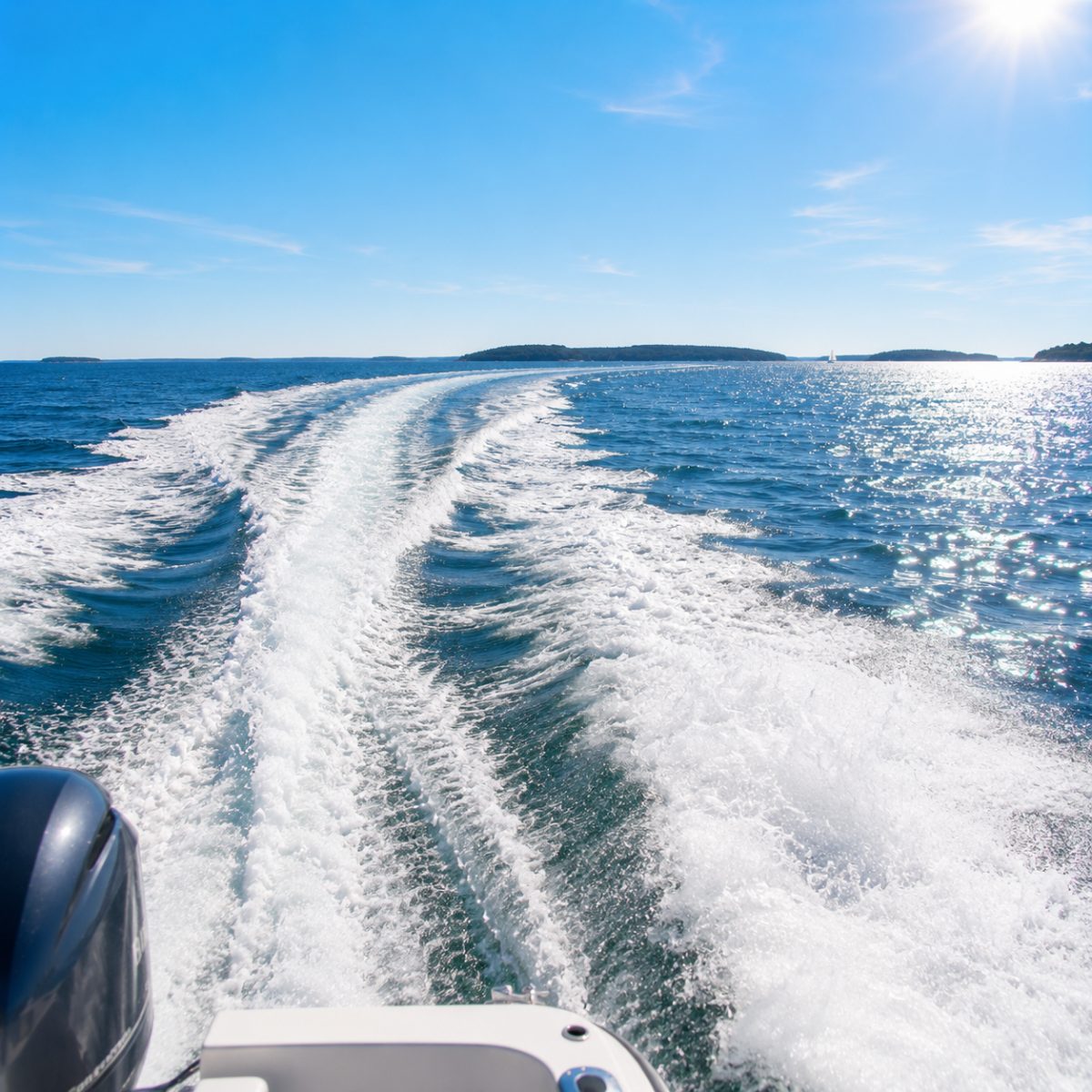The boat's white wake curving across sparkling deep-blue water toward the horizon