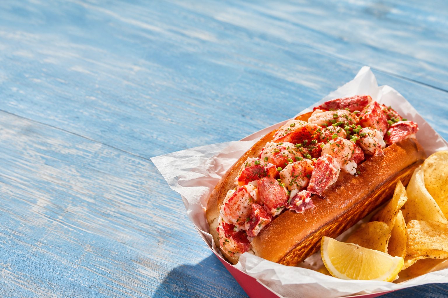 Classic Maine cold lobster roll in a red paper boat with lemon and chips